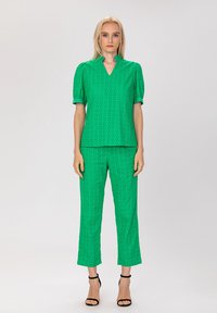 Haut vert à manches courtes avec un décolleté en V et des manches bouffantes, associé à un pantalon court assorti. Les deux présentent un motif texturé.