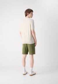 Maglioncino corto beige a maniche corte con texture abbinato a pantaloni corti verdi, sneakers bianche e calze bianche. Design semplice senza motivi visibili.