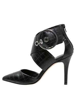 Chaussure à talon haut noire avec un bout pointu, en cuir à motif crocodile texturé, dotée d'une bride à la cheville avec un accent circulaire argenté.