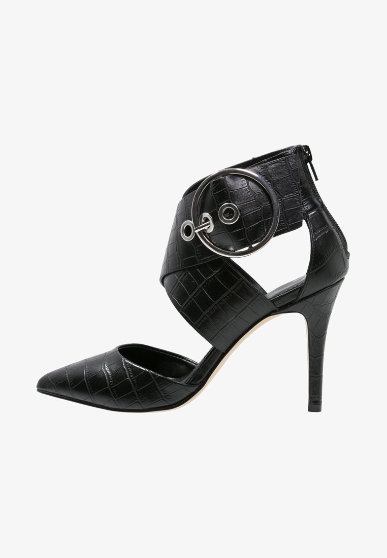 Chaussure à talon haut noire avec un bout pointu, en cuir à motif crocodile texturé, dotée d'une bride à la cheville avec un accent circulaire argenté.