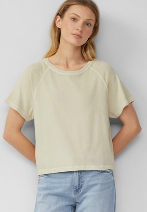 Top a maniche corte, collo tondo in tessuto beige chiaro con una texture morbida. Presenta una vestibilità ampia e maniche raglan.