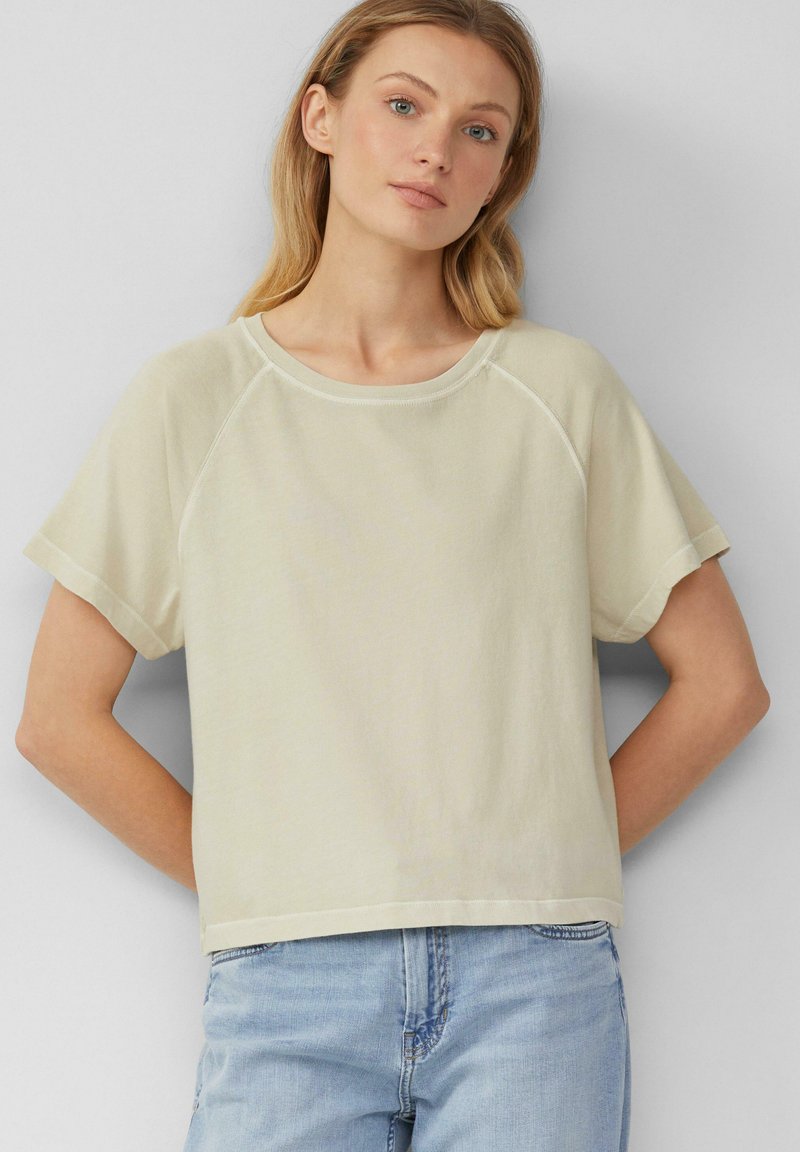 Top a maniche corte, collo tondo in tessuto beige chiaro con una texture morbida. Presenta una vestibilità ampia e maniche raglan.