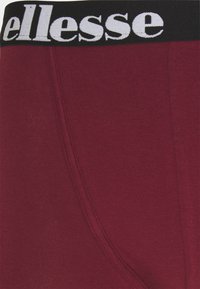 Burgundy boxershorts med svart midjeband som har varumärkesnamnet i vit text. Mjuk tyg med slät yta och sömnadsdetaljer.