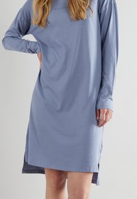 Abito azzurro chiaro a maniche lunghe con vestibilità ampia, caratterizzato da spacchi laterali e un logo discreto sul petto. Tessuto di cotone morbido.