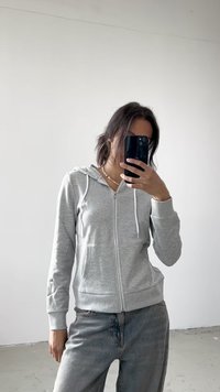 Sweatshirt cinza com fecho de correr, capuz com cordão, punhos canelados e uma textura suave, usado com jeans de lavagem clara.