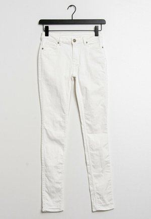 Białe dżinsy skinny na czarnym wieszaku. Posiadają zapięcie na guzik z przodu, pięć kieszeni oraz gładką, lekko teksturowaną tkaninę.