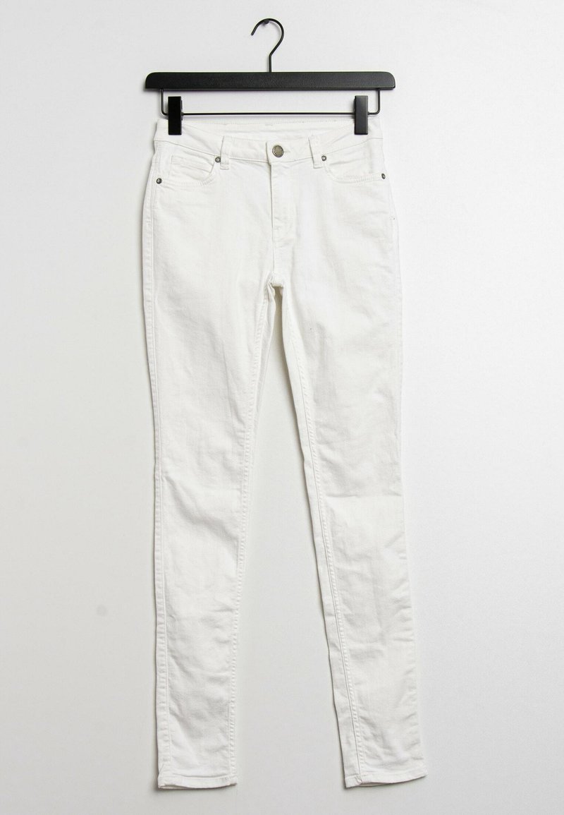 Jeans skinny de mezclilla blanca en un perchero negro. Cuenta con un cierre de botón frontal, cinco bolsillos y una tela suave, ligeramente texturizada.