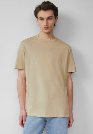 Beige t-shirt met korte mouwen in zachte stof, met een ronde halslijn en subtiele logo-details op de voorkant. Gecombineerd met lichtblauwe spijkerbroek.