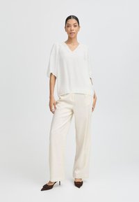 Blusa blanca texturizada con escote en V y detalles de encaje, combinada con pantalones de pierna ancha color crema y tacones marrones puntiagudos. Diseño simple y elegante.