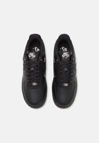 Ζευγάρι μαύρων sneakers Nike Air Force 1 με κορδόνια, τρυπητά μποξαρισμένα δάχτυλα και λογότυπο Nike Air στην γλώσσα και τις σόλες, απεικονιζόμενο από πάνω.