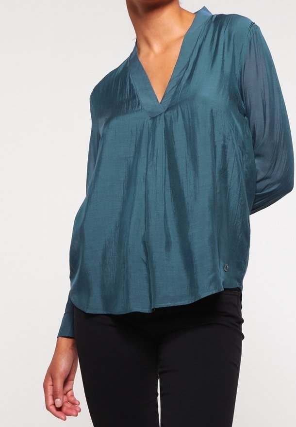 Blusa teal con scollo a V, maniche lunghe e vestibilità comoda; realizzata in un tessuto morbido e lucido; presenta una trama sottile e un orlo arrotondato.