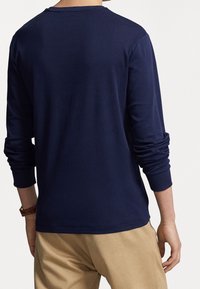 Tmavě modré tričko s dlouhým rukávem a kulatým výstřihem, vyrobené z měkkého materiálu, se šitými manžetami a hladkým, jednobarevným vzhledem.