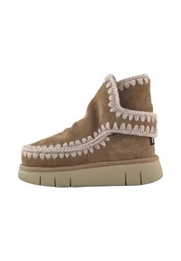 Bottes cheville en daim marron avec un dessus pelucheux, des coutures détaillées et un accent crème texturé le long du bord, reposant sur une semelle épaisse beige.