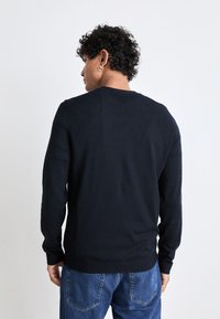 Svart stickad tröja med rund hals, långa ärmar och ribbad nederkant. Stylad med blå denimjeans som visar en jämn textur.