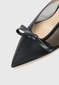 Black pointed-toe shoe with a textured upper and sheer mesh sides, featuring a small bow accent on the vamp. Smooth inner lining.