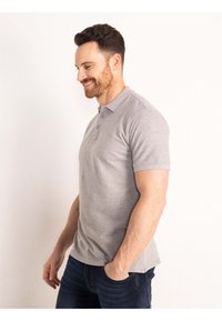 Grijze polo met korte mouwen, drie knopen bij de hals en zachte katoenen stof. G gedragen met donkerblauwe jeans. Eenvoudig ontwerp, geen patronen.