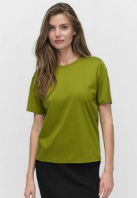 Kortärmad t-shirt med rund hals i livfullt grönt tyg, mjuk textur med avslappnad passform, ihop med en plisserad svart kjol.