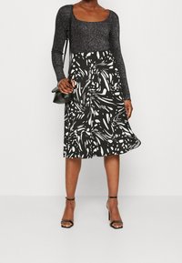 Falda vaporosa en blanco y negro con patrones abstractos, combinada con una blusa oscura de manga larga y brillantes. Accesorios incluyen un pequeño bolso negro.