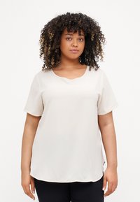 Cream-colored short-sleeve blouse with a scoop neckline, featuring a smooth, lightweight fabric and a slightly curved hem.