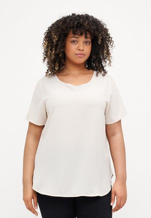 Cream-colored short-sleeve blouse with a scoop neckline, featuring a smooth, lightweight fabric and a slightly curved hem.