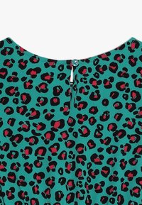 Kleid mit Leopardenmuster auf türkisfarbenem Grund, das schwarze und rote Flecken aufweist. Rückseite mit einem Knopf- und Schlaufenverschluss versehen. Glatte Textur.