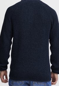 Marineblauer Strickpullover mit strukturiertem Gewebe, Raglanärmeln und gerippten Bündchen. Lässige Passform mit geradem Saum, getragen über blauen Jeans.