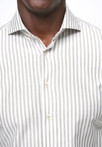 Camisa de cuello en gris claro y blanco con rayas verticales, que presenta un diseño clásico abotonado con botones beige y una textura de tela suave.
