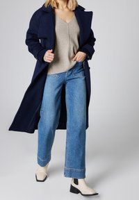 Marinblå ullkappa med breda slag, ljusgrå v-ringad tröja, högmidjade blå jeans och krämfärgade ankelstövlar med svarta klackdetaljer.