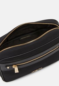 Borsa in pelle nera con zip superiore e hardware dorato, include una tasca frontale con zip. L'interno è foderato in tessuto con un'etichetta logo.