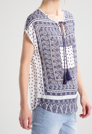 Sømandsblå og hvid mønstret skjorte med korte ærmer, V-hals og frynsebinding. Har geometriske og blomstrede designs over hele skjorten.