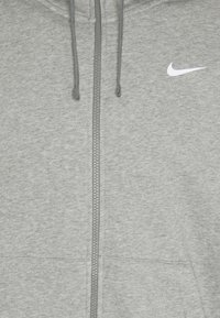 Grå zip-up hoodie i texturerad tyg. Har en framdragkedja, två nederfickor och en liten vit Nike-logga på bröstet.