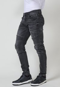 Fekete, skinny farmernadrág, bordázott térdakkordokkal és enyhe fényességgel. Denim anyagból készült, hagyományos zsebekkel és fitted kialakítással.