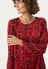 Rød kjole med sort leopardprint, med lange ærmer og rund halsudskæring. Glat stof med en afslappet pasform og let drapering.