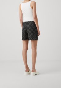 Černé vzorované šortky s bílými geometrickými motivy, spárované s bílým tílkem a světlými platformovými sandály.