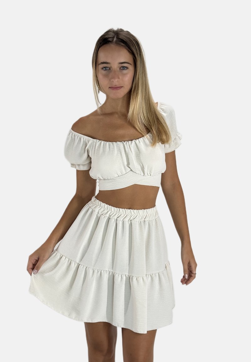 Zweiteiliges Outfit, bestehend aus einem kürzeren, schulterfreien Oberteil und einem ausgestellten, gestuften Rock. Hergestellt aus einem leichten, strukturierten, hellen Creme-Stoff.