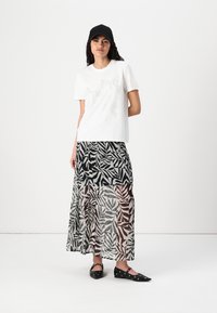 Vit t-shirt med ett dekorativt tryck och en svart, genomskinlig maxikjol med ett tropiskt bladmönster i svarta och grå nyanser. Svarta ballerinas.