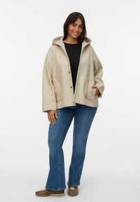 Beige hættejakke med en afslappet pasform, der har trykknapper og to forlommer. Bæret over en sort top og parret med blå flagrende jeans.