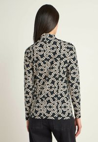Long-sleeve top featuring a geometric black and beige pattern, made from a smooth fabric, with a high neckline and slim fit.
