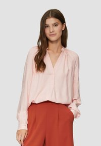 Lichtroze blouse met lange mouwen, een V-hals en geplooide schouders, gecombineerd met roestkleurige high-waisted broek. Gladde stof, comfortabele pasvorm.