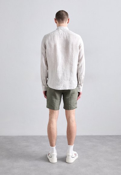 Camasa lungă din in bej deschis, pantaloni scurți din in verzi, adidași albi cu accente roșii și șosete albe. Design simplu, croi lejer.