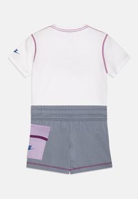 Camisa blanca de manga corta con detalles en púrpura y pantalones cortos grises que presentan un parche púrpura. Tejido suave con detalles de costura en contraste.