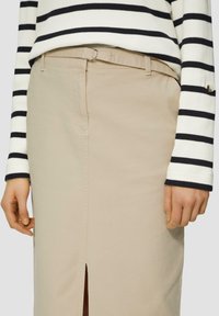 Jupe beige avec une fente avant, faite en tissu, accompagnée d'un pull côtelé rayé noir et blanc avec un détail de bouton à la manche.
