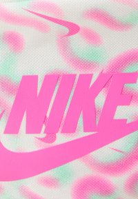 Nike logó merész, címkézett, rózsaszín betűkkel egy fehér, mintázott háttér előtt, amely pasztell rózsaszín és zöld örvényekből áll, texturált anyagból.