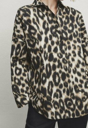 Koszula z długim rękawem i kołnierzykiem w czarno-beżowy wzór lamparta, noszona na czarnych spodniach.