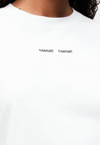 White cotton T-shirt with a round neckline. Features black embroidered text "SAMÆØ SAMSØE" on the front. Smooth texture, regular fit.