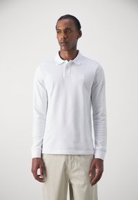 Cămașă polo albă cu mâneci lungi, confecționată din bumbac, având un guler clasic, o placket cu două butoane și un mic patch cu logo pe piept.