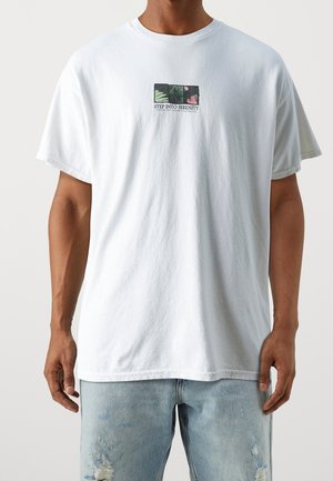 Weißes Baumwoll-T-Shirt mit einem Frontgrafikdruck, auf dem der Text "STEP INTO SERENITY" sowie abstrakte Bilder innerhalb eines rechteckigen Rahmens zu sehen sind.