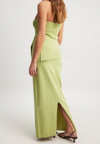 Utan axelband grön maxiklänning i en texturerad tyg, med sidoslitsdetalj, åtsittande liv och avslappnad kjol. Minimalistisk design.