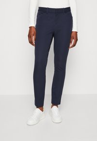 Meriinoblå dressbyxor med smal passform, bältesöglor och sidofickor. Kombinationen med vita sneakers ger en ren och modern look.