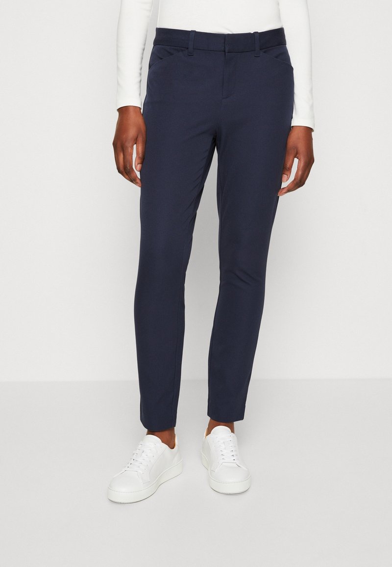 Meriinoblå dressbyxor med smal passform, bältesöglor och sidofickor. Kombinationen med vita sneakers ger en ren och modern look.